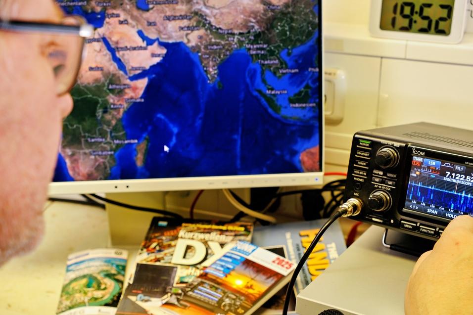 eine mänliche Person mit Brille sitzt vor einem Monitor der eine Weltkarte zeigt, die Person bedient ein KW-Funkgerät, auf dem Display ist das 40m Band eingestellt eine mänliche Person mit Brille sitzt vor einem Monitor der eine Weltkarte zeigt, die Person bedient ein KW-Funkgerät, auf dem Display ist das 40m Band eingestellt