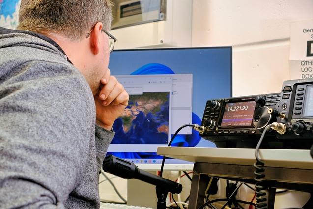 eine mänliche Person sitz vor einem Kurzwellenfunkgerät, die rechte Hand ist vor dem Gesicht, er blickt auf einen Monitor auf dem Bildschirm ist eine Weltkarte zu sehen! eine mänliche Person sitz vor einem Kurzwellenfunkgerät, die rechte Hand ist vor dem Gesicht, er blickt auf einen Monitor auf dem Bildschirm ist eine Weltkarte zu sehen!