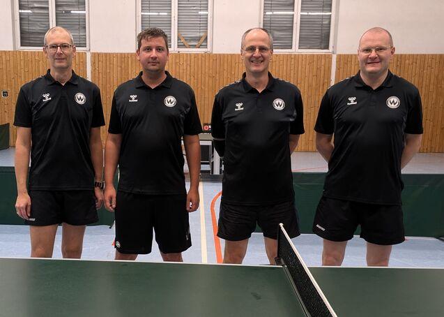 Vier Männer in schwarzen Trikots an einer Tischtennisplatte.