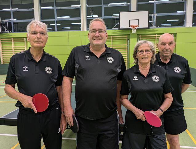 Eine Frau und drei Männer in schwarzen Trikots an einer Tischtennisplatte