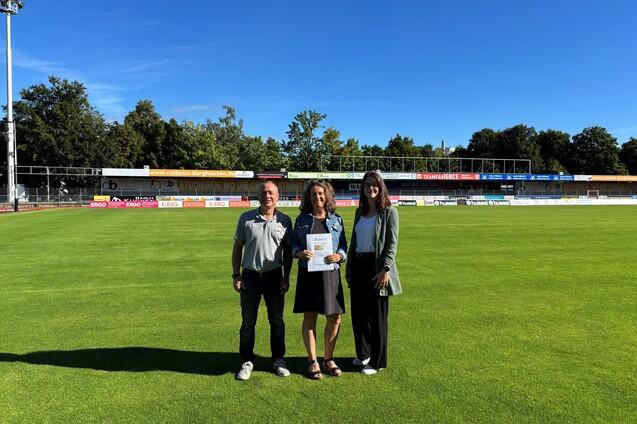 das Bild zeigt Geschäftsführer Heiko Hiller, Michaela Hausmann sowie Vereinsmanagerin Laura König, bei der Übergabe der goldenen Ehrenamtskarte für 25 Jahre ehrenamtliche Tätigkeit