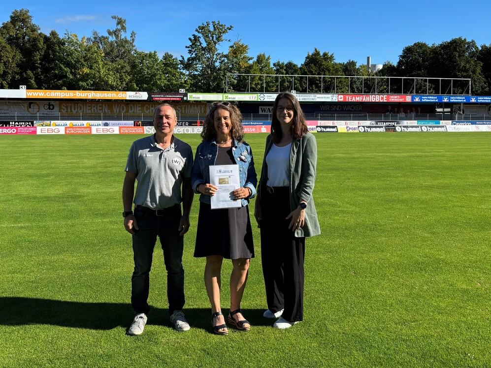 das Bild zeigt Geschäftsführer Heiko Hiller, Michaela Hausmann sowie Vereinsmanagerin Laura König, bei der Übergabe der goldenen Ehrenamtskarte für 25 Jahre ehrenamtliche Tätigkeit