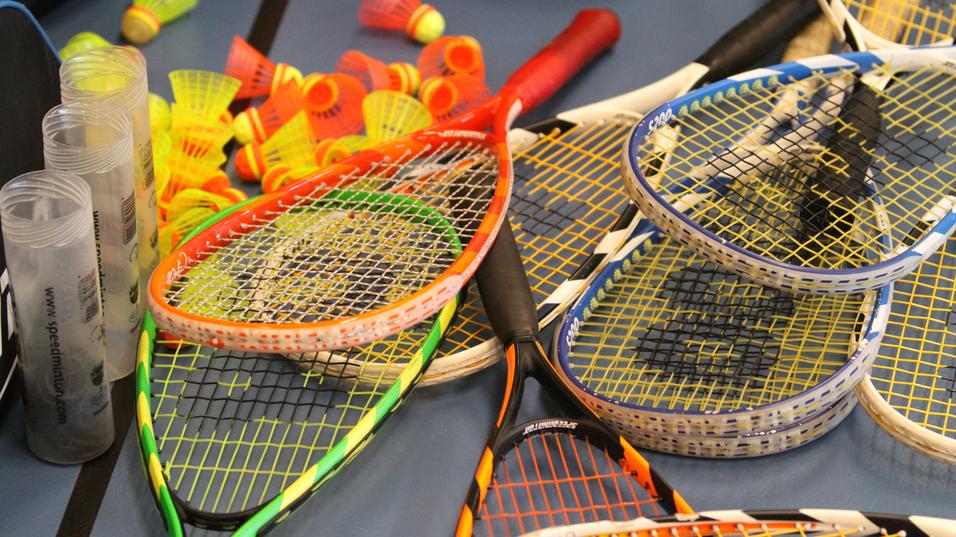 Bunte Badminton-Schläger und -Bälle liegen auf einem Tisch, umgeben von transparenten Schutzhüllen.