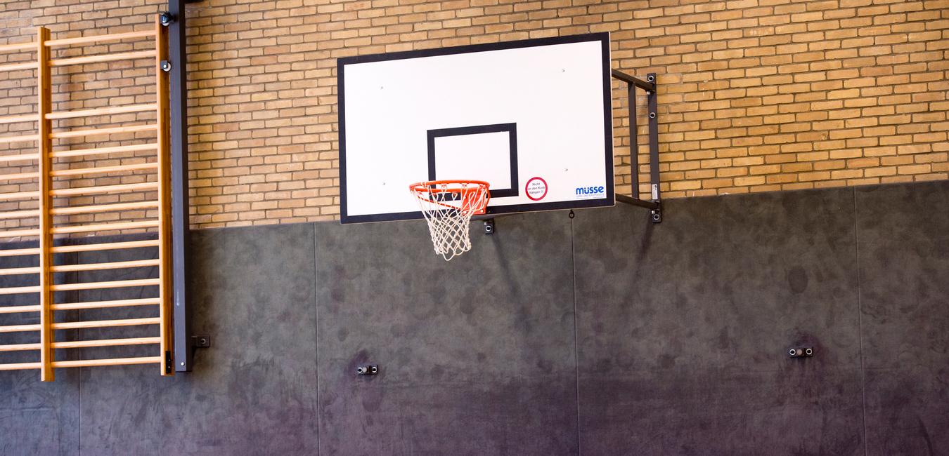 Basketballkorb an einer Wand mit Sprossenwand im Hintergrund in einer Sporthalle.