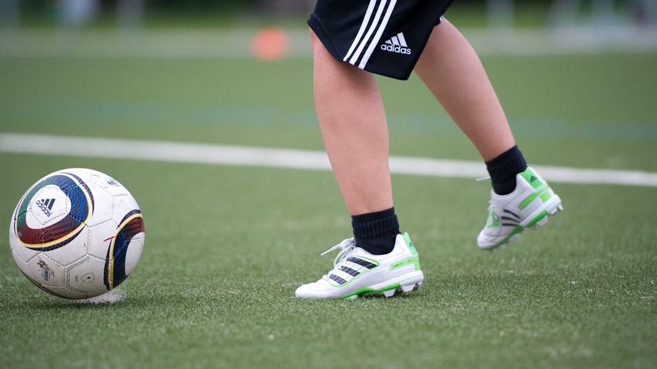 Ein Fuß mit Fußballschuhen tritt auf einen Fußball auf einem Kunstrasenfeld.