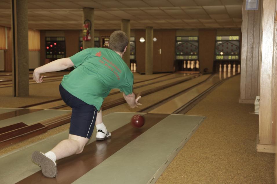 Ein Spieler beugt sich vor, um eine Bowlingkugel auf einer Bahn in einem Bowlingsalon zu werfen.
