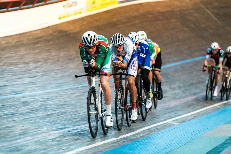 Gruppe von Radrennfahrern in bunten Trikots auf einer Holzbahn während eines Velodrom-Rennens.