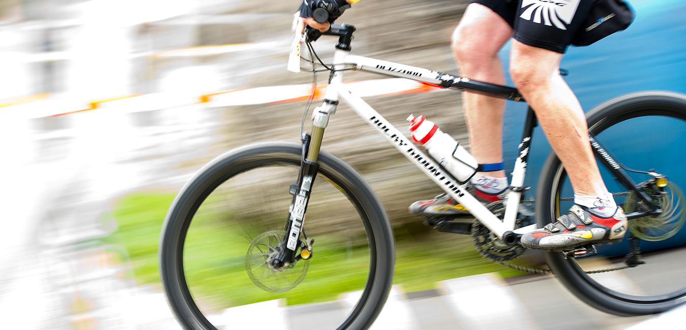 Radsportler fährt mit einem Mountainbike auf einem unebenen Terrain, Wasserflasche am Rahmen, schnelle Bewegung.