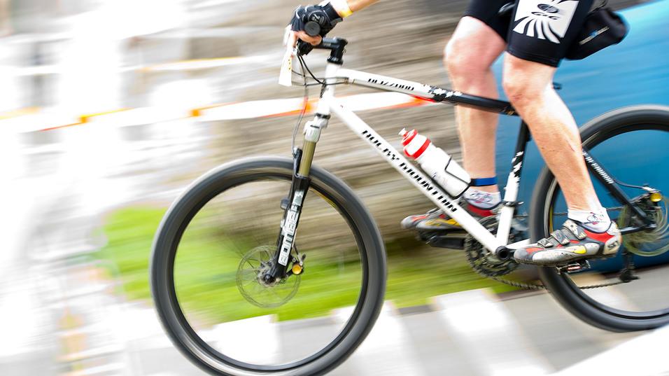 Radsportler fährt mit einem Mountainbike auf einem unebenen Terrain, Wasserflasche am Rahmen, schnelle Bewegung.