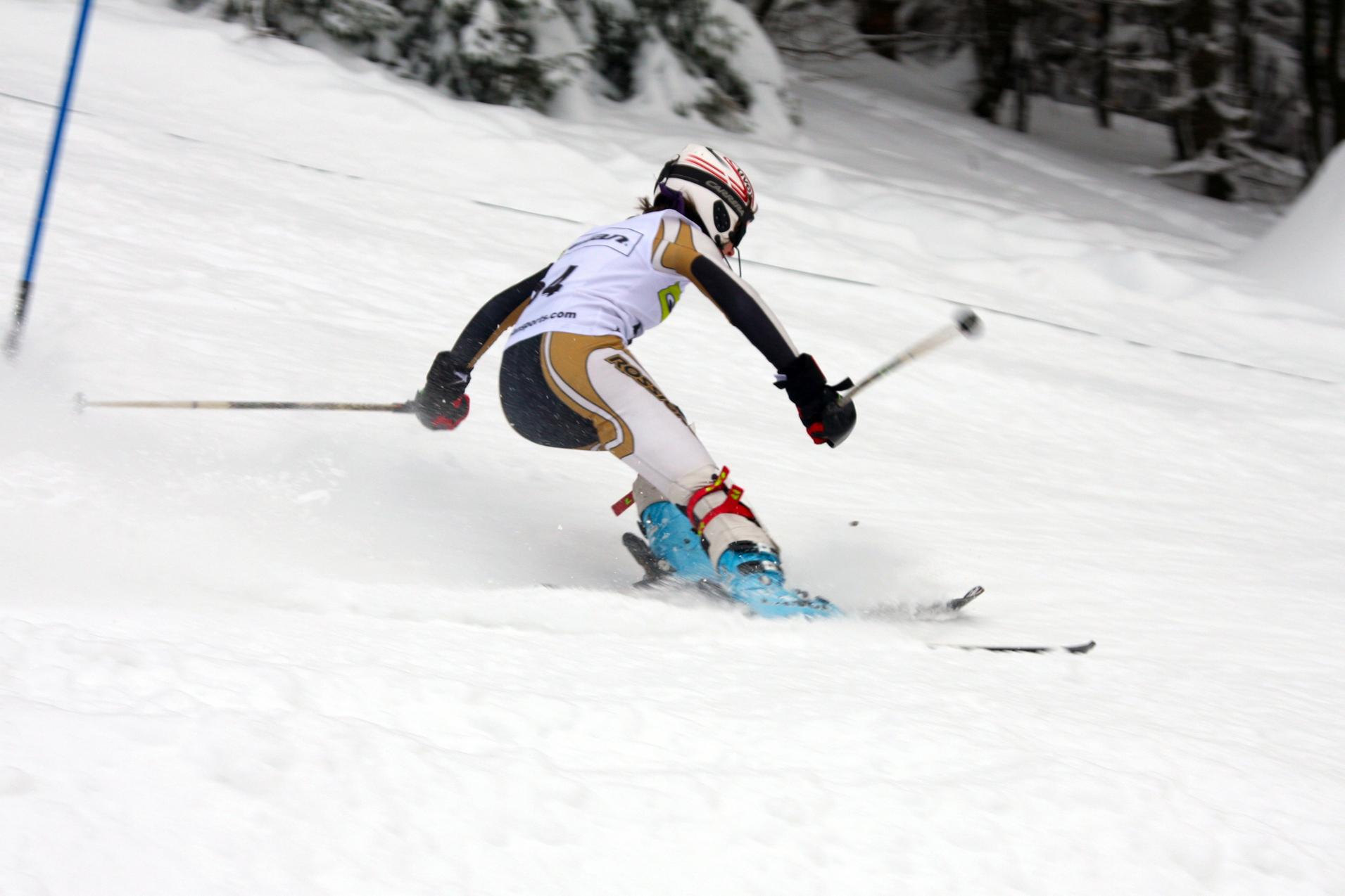 Skifahrer in voller Fahrt bei einem Wettkampf, mit Skistöcken auf einer verschneiten Piste.