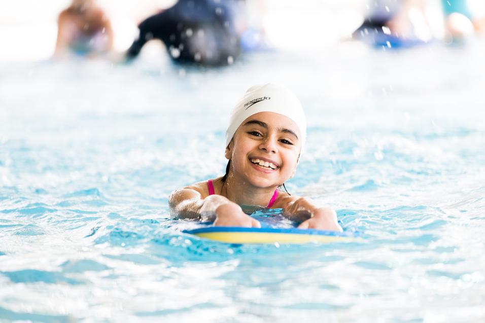 Kind schwimmt mit Schwimmbrett